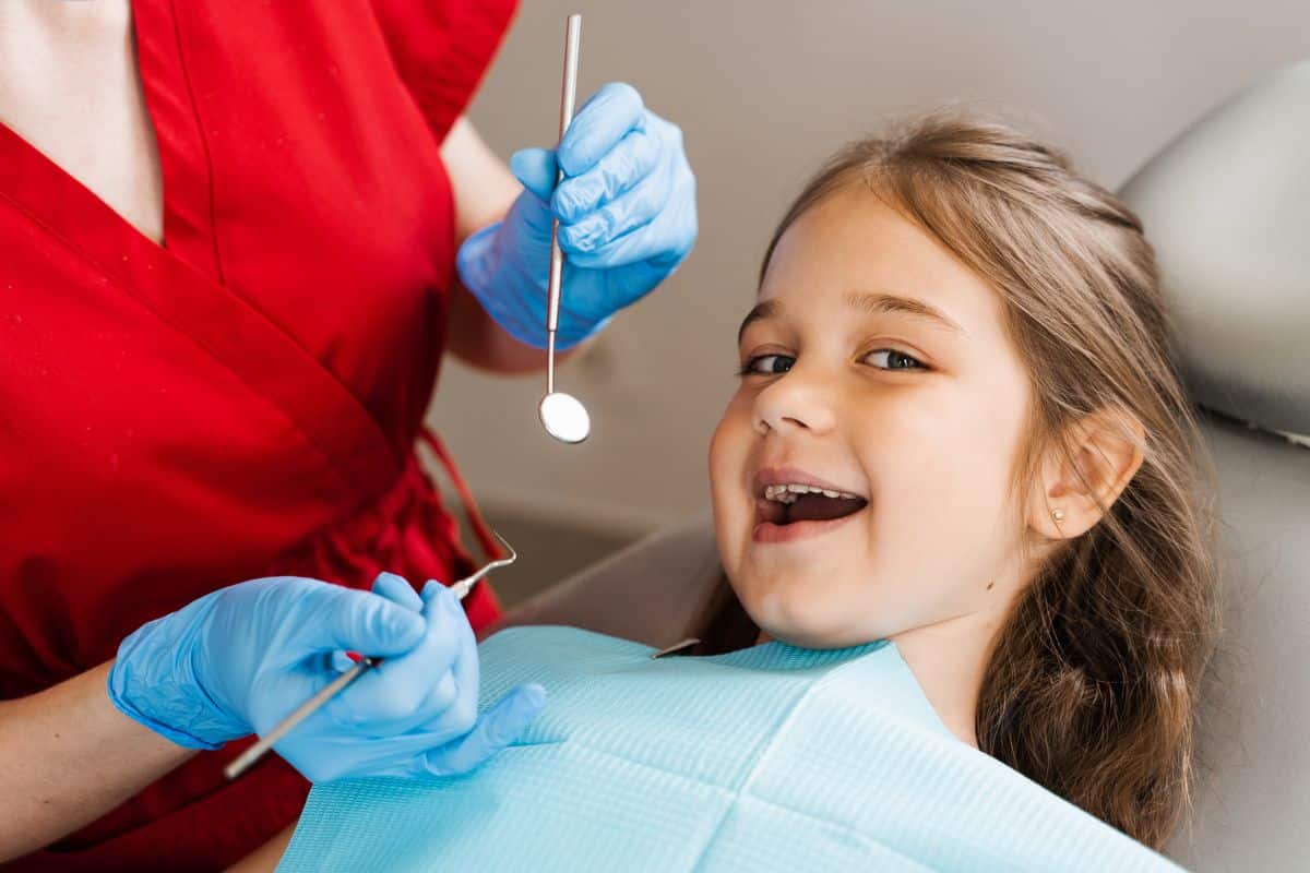 Child smiling during a dental checkup to monitor a loose baby tooth.